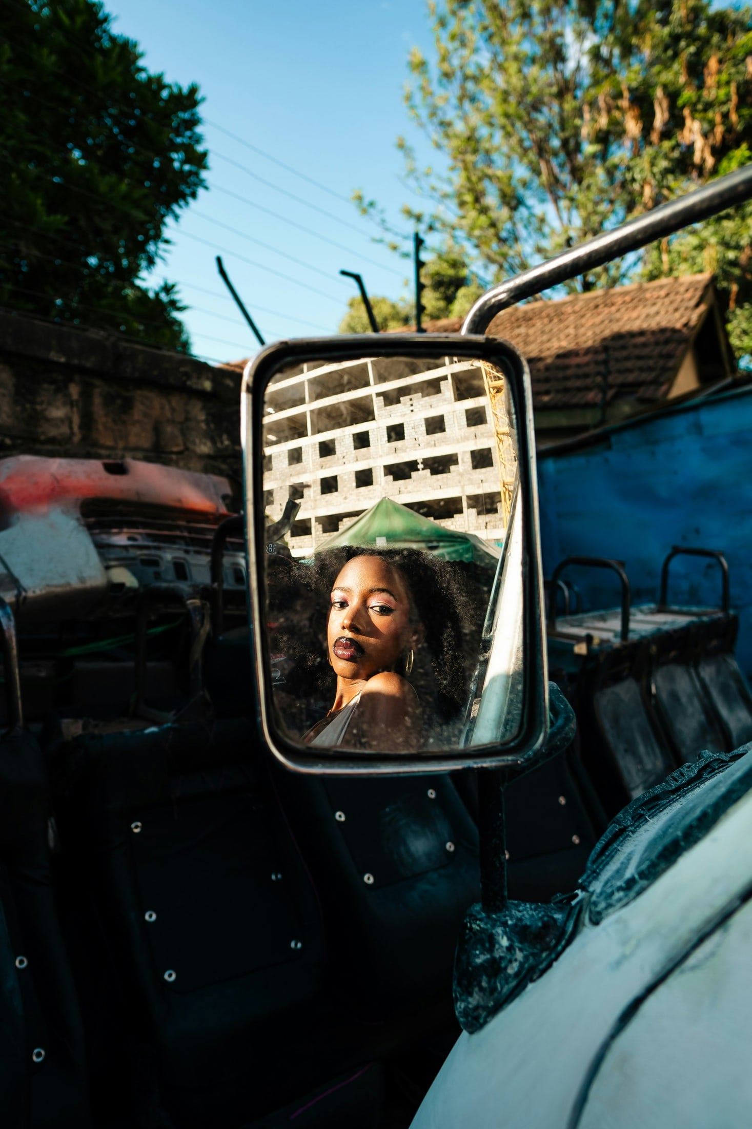 A woman's face framed in the side mirror of an open-top vehicle under a blue sky.