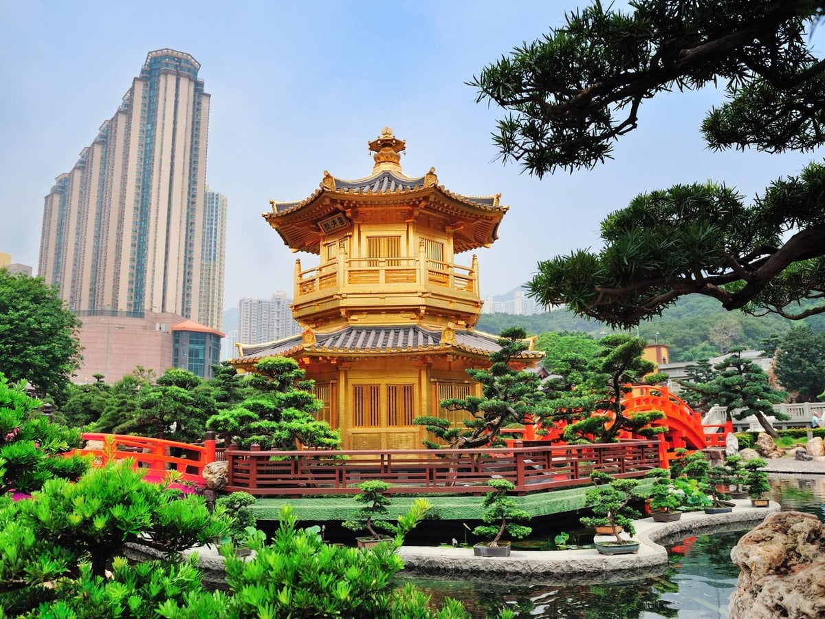 A golden pavilion in a Hong Kong garden, with pines, a red bridge and towers behind.