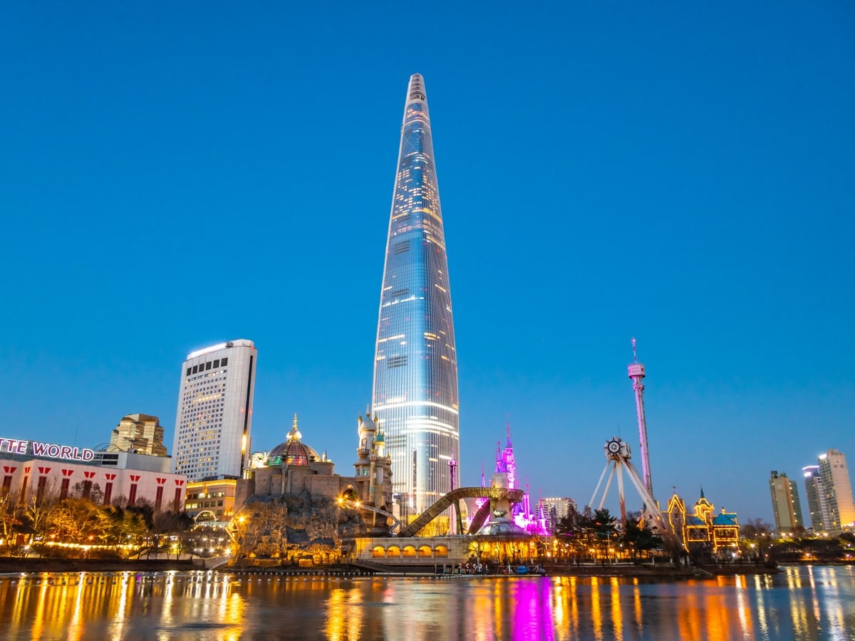 Seoul at dusk, a tall glass tower above lights reflected in a lake.